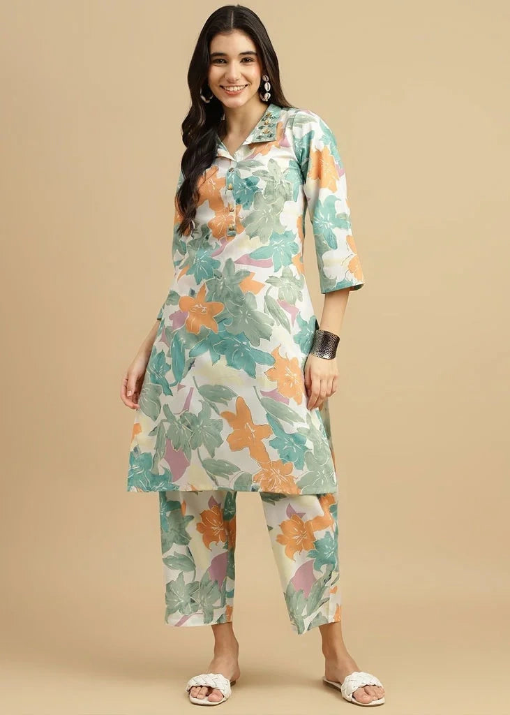 Woman wearing a pink cotton‑rayon floral print kurta and matching straight pants; kurta features a round neckline, three‑quarter sleeves, calf‑length hem, and a flowy a‑line silhouette with side slits.