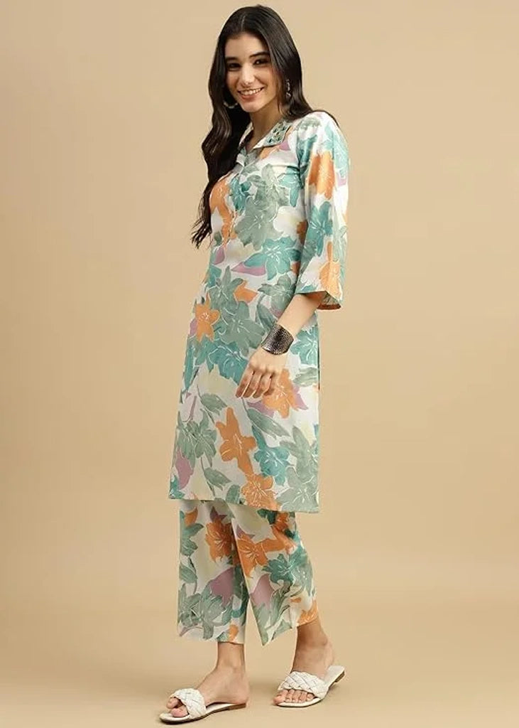 Woman wearing a pink cotton‑rayon floral print kurta and matching straight pants; kurta features a round neckline, three‑quarter sleeves, calf‑length hem, and a flowy a‑line silhouette with side slits.