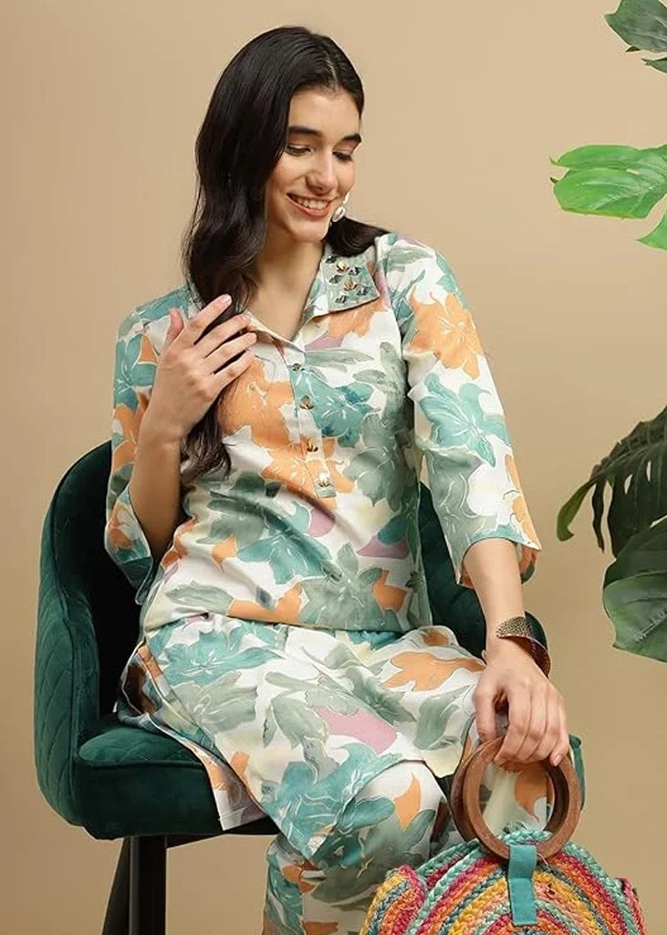 Woman wearing a pink cotton‑rayon floral print kurta and matching straight pants; kurta features a round neckline, three‑quarter sleeves, calf‑length hem, and a flowy a‑line silhouette with side slits.