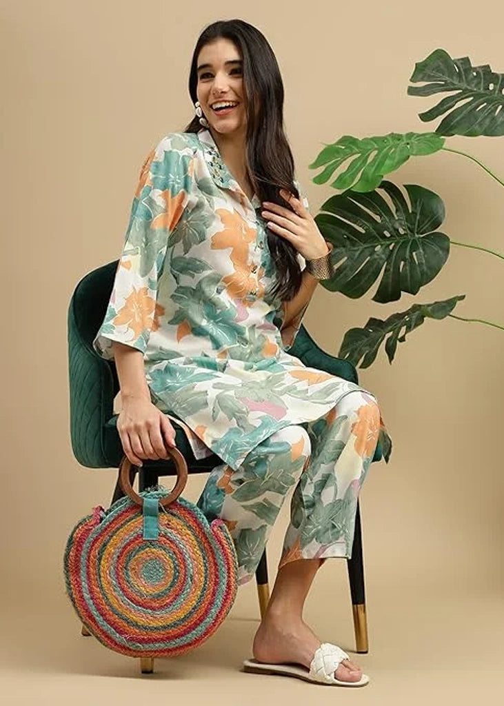 Woman wearing a pink cotton‑rayon floral print kurta and matching straight pants; kurta features a round neckline, three‑quarter sleeves, calf‑length hem, and a flowy a‑line silhouette with side slits.
