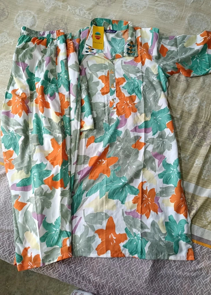 Woman wearing a pink cotton‑rayon floral print kurta and matching straight pants; kurta features a round neckline, three‑quarter sleeves, calf‑length hem, and a flowy a‑line silhouette with side slits.