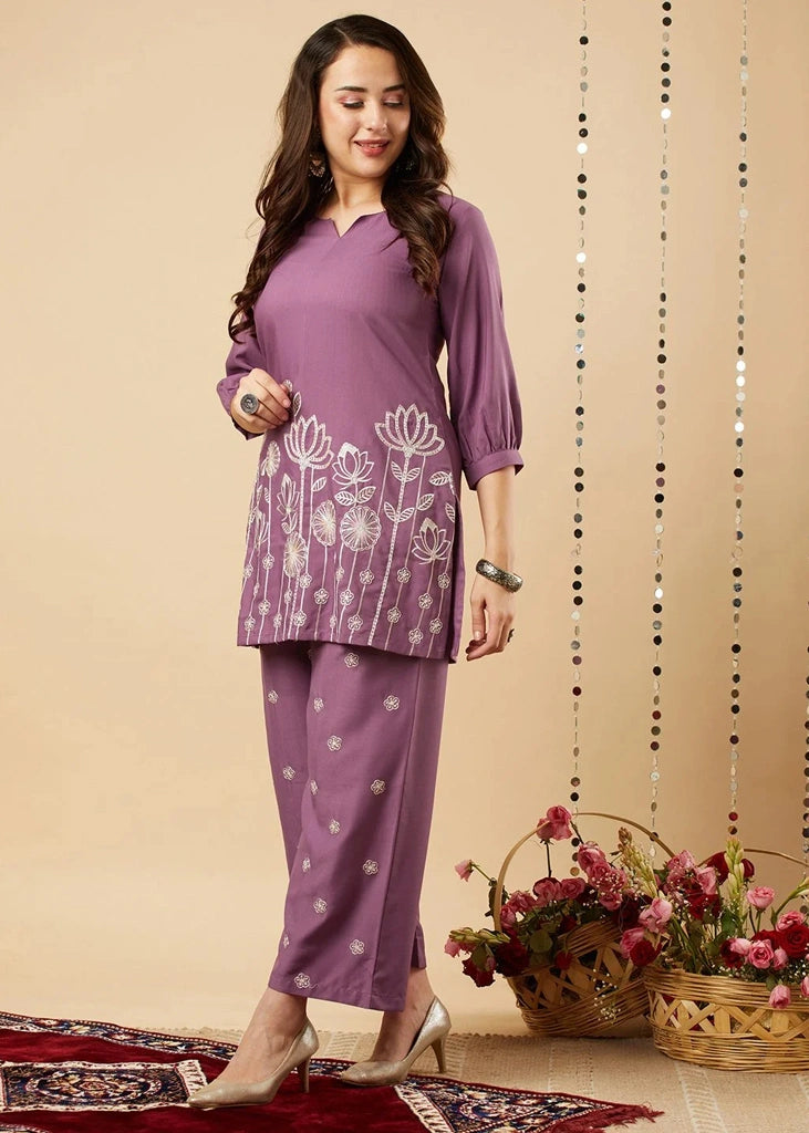 Women's lavender kurta-and-pant set in lightweight fabric, featuring intricate white floral embroidery across the front, with a round neckline, three-quarter sleeves, straight pants, and a streamlined, elegant silhouette.