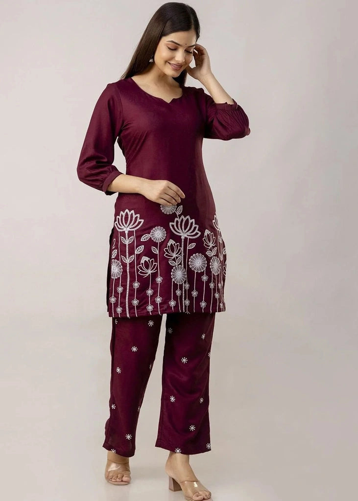 Women's Maroon kurta-and-pant set in lightweight fabric, featuring intricate white floral embroidery across the front, with a round neckline, three-quarter sleeves, straight pants, and a streamlined, elegant silhouette.
