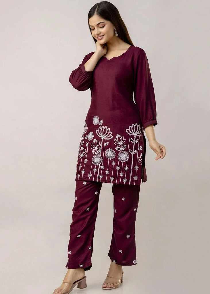 Women's Maroon kurta-and-pant set in lightweight fabric, featuring intricate white floral embroidery across the front, with a round neckline, three-quarter sleeves, straight pants, and a streamlined, elegant silhouette.