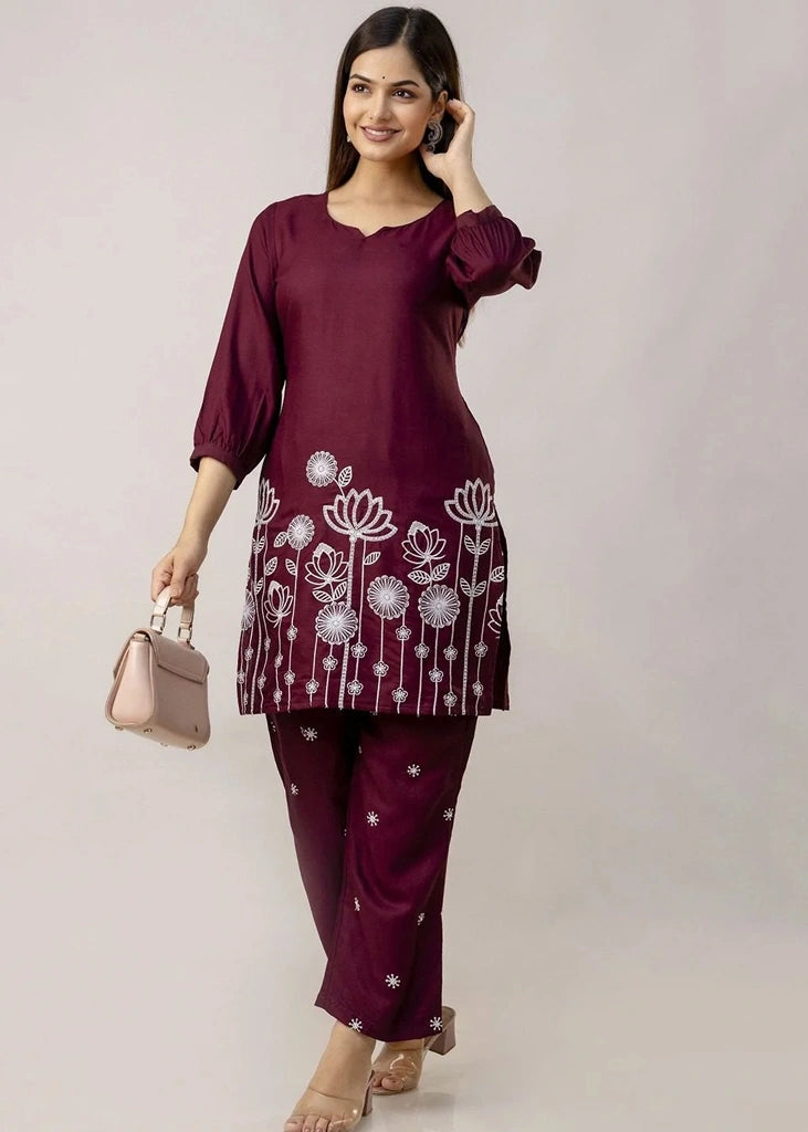 Women's Maroon kurta-and-pant set in lightweight fabric, featuring intricate white floral embroidery across the front, with a round neckline, three-quarter sleeves, straight pants, and a streamlined, elegant silhouette.