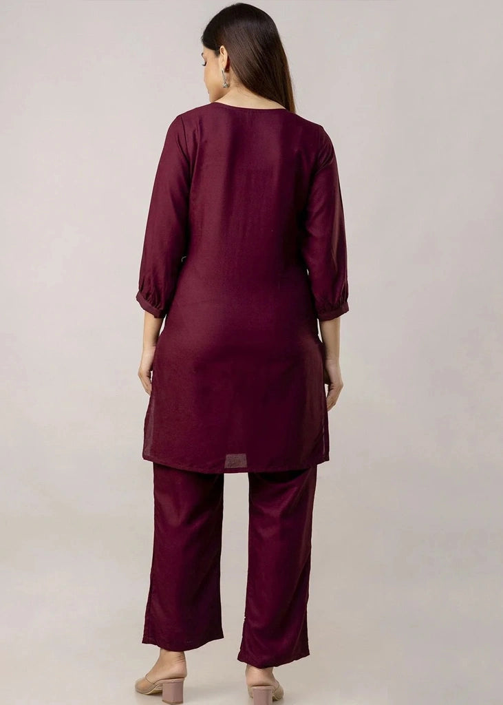 Women's Maroon kurta-and-pant set in lightweight fabric, featuring intricate white floral embroidery across the front, with a round neckline, three-quarter sleeves, straight pants, and a streamlined, elegant silhouette.